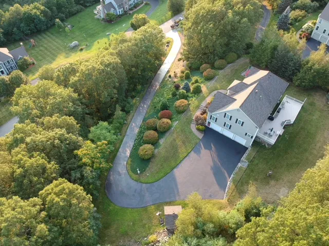 Aerial view of a perfectly sealcoated property, showing the contrast between the deep black asphalt and the lush green landscape of a typical Acton, MA home.