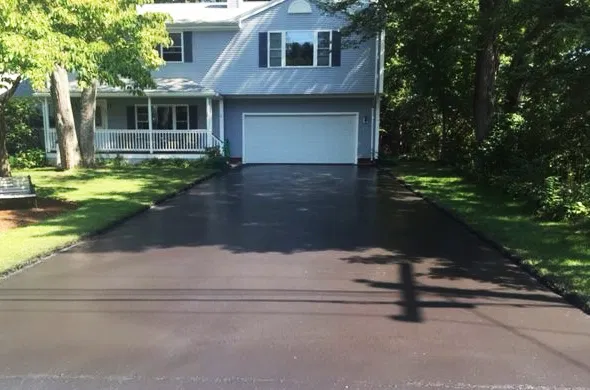 A close-up of a perfectly sealed residential driveway in front of a two-car garage in Maynard MA